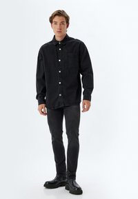 Camisa de mezclilla negra con diseño abotonado, un bolsillo en el pecho y puños. Combinada con jeans negros ajustados y botas negras robustas.