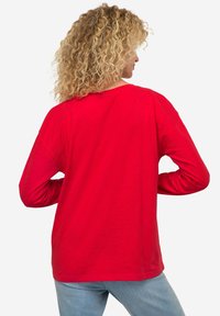 Rotes langärmliges T-Shirt mit Rundhalsausschnitt, lässiger Passform und gerippten Bündchen, aus weichem Stoff, von hinten gezeigt, mit sichtbarem blonden lockigem Haar.