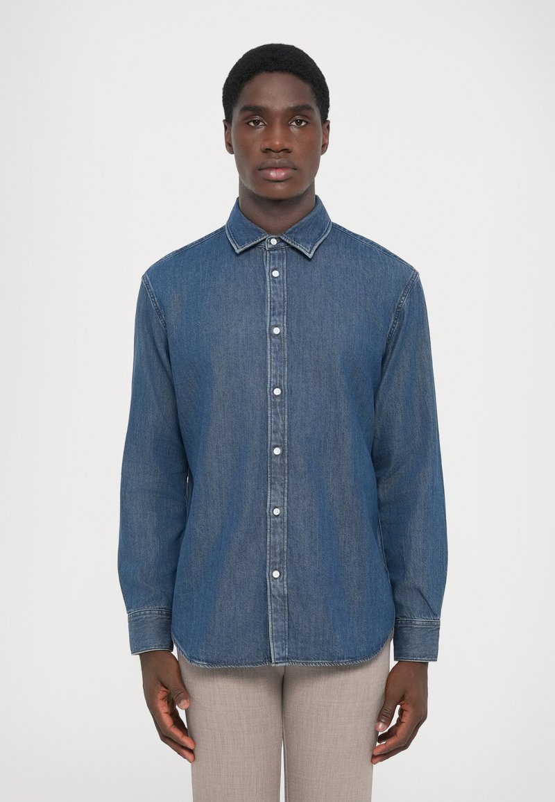 Chemise en denim bleu foncé avec un col, des manches longues, une fermeture à boutons, des surpiqures contrastées et un ourlet droit.