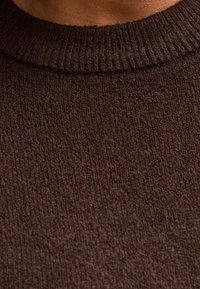 Suéter marrón con un patrón de punto texturizado y cuello de canalé. La tela parece suave y cálida, con tonos marrones variados.