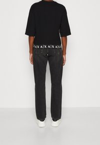 Černá mikina s ohrnutými rukávy, s bílým grafickým pruhem na spodním lemu. Spárována s tmavými džíny a bílými teniskami.