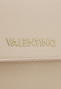 Beige texturerad läderplånbok med en guldfärgad "VALENTINO"-logotyp som är tydligt synlig på framsidan. Sömmen synlig längs kanterna.