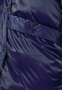 Tume sinine puhvjakas, millel on sile ja läikiv tekstuur, horisontaalne tikandikujundus ning suured nööbid ees ja külgedel.