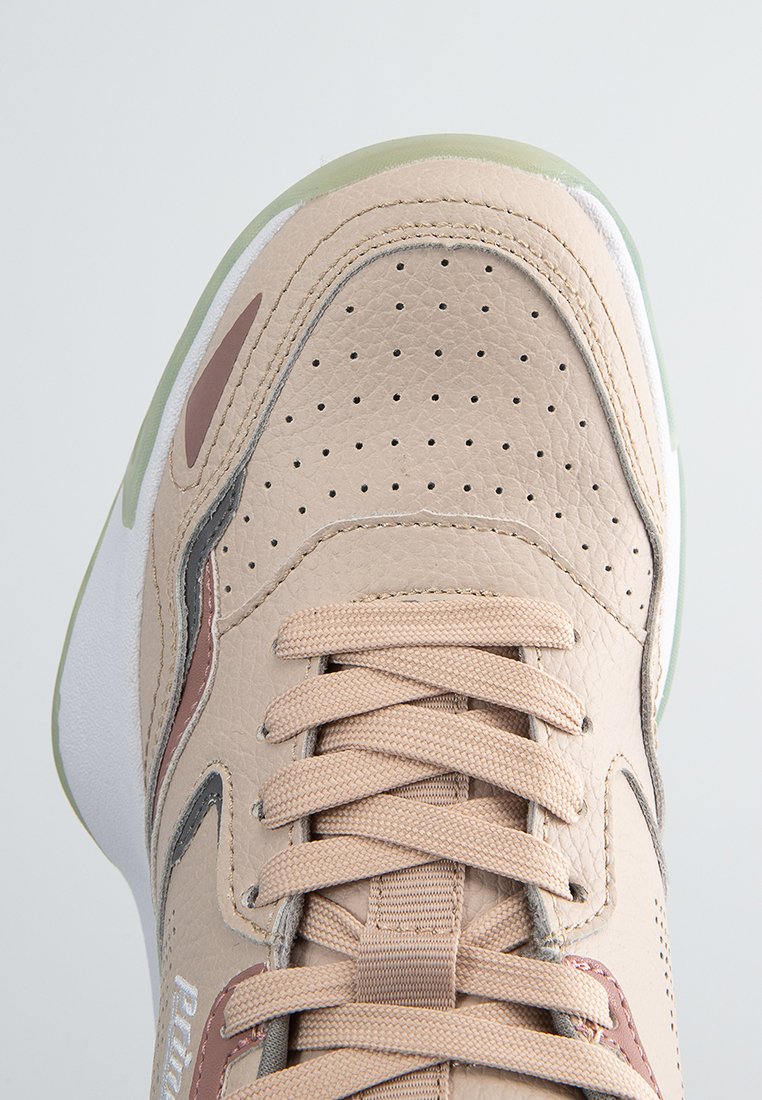 Zapatilla con cordones en cuero beige claro con textura perforada, acentos grises y suela verde. Presenta un collar acolchado y detalles de costura.