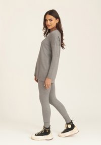 Grey long-sleeve top paired with grey leggings, both made of soft fabric. Worn with black high-top sneakers featuring white soles.