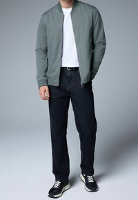 Chaqueta bomber gris claro sobre una camiseta blanca, combinada con vaqueros azul oscuro y zapatillas negras con detalles en blanco. Diseño simple, cierre con cremallera.