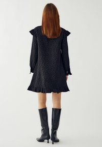 Czarna sukienka z teksturowanym florystycznym wzorem, długimi rękawami z falbanami i rozkloszowanym dołem. Połączona z czarnymi botkami do kolan.