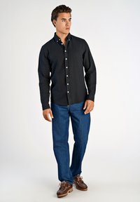 Dunkelblaues Hemd mit Knopfleiste und spitzem Kragen, kombiniert mit blauen Jeans und braunen Bootsschuhen. Der Stoff wirkt weich und leicht strukturiert.