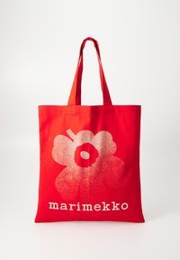 Piros szövet bevásárlótáska, amelyen egy nagy fehér virágminta található, valamint a "marimekko" felirat fehér színben az alján. Két strapabíró füllel.