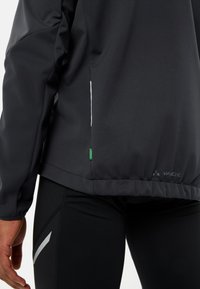 Giacca nera realizzata in materiale liscio e resistente all'acqua, con una vestibilità aderente. Presenta accenti bianchi e un'etichetta verde sul bordo.