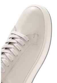 Sneaker en cuir gris clair avec bout rond, lacets plats et semelle blanche contrastante. Texture lisse avec de subtils détails de couture.