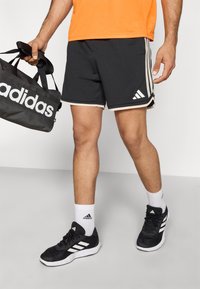 Black athletic shorts with light gray trim, three white stripes down the sides, paired with black sneakers, white socks, and a black duffle bag.