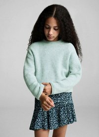 Ljusgrön ribbad stickad tröja med långa ärmar, i kombination med en mörk blommönstrad utsvängd kjol. Mjuk textur, avslappnad design.