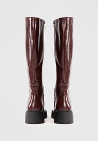 Knee-high burgundské kožené čižmy s lesklým povrchom, bočnými zipsami a čiernymi robustnými podpätkami. Hladká textúra s vystuženými švami.