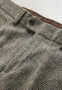 Trousers made of textured, woven fabric in shades of brown and gray, featuring a single brown button and a hidden zipper closure.