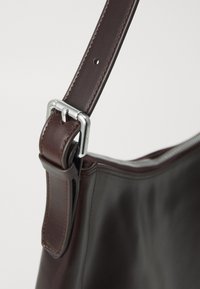 Adjustable dark brown leather bag strap with silver buckle and stitched edges, attached to smooth leather bag body.
