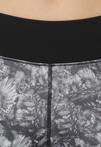 Czarne legginsy z wysokim stanem z szarym abstrakcyjnym wzorem. Materiał jest elastyczny o gładkiej fakturze i zawiera płaskie szwy.