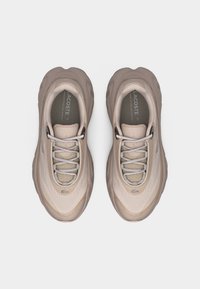 Paire de baskets Lacoste beige avec semelles arrondies, empeignes en mesh et lacets, photographiées de dessus sur un fond uni.