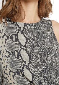 Ärmlös topp med ett mönster i ormskinn i nyanser av svart och beige, med en strukturerad tygkvalitet och en rund halsringning.