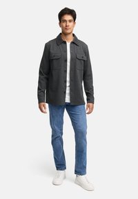 Grå knap-op skjorte i en uldblanding med to brystlommer, parret med lyseblå jeans og hvide sneakers på en ensfarvet baggrund.