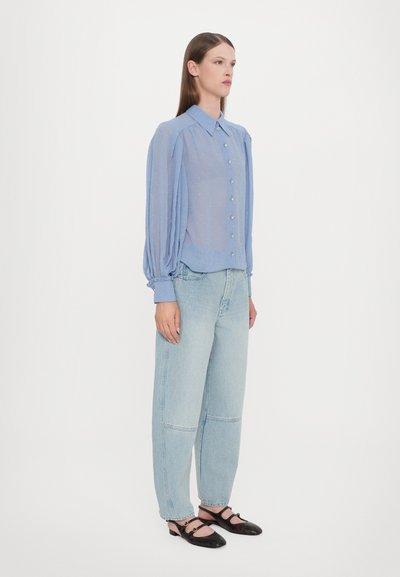 Light blue sheer blouse with button closure, puffed long sleeves, and a smooth texture; paired with loose light denim jeans and black shoes.