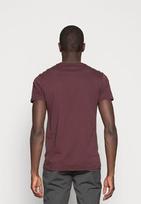 Burgundské bavlněné tričko s krátkým rukávem, kulatým výstřihem a hladkou texturou; zobrazeno zezadu na jednobarevném bílém pozadí.