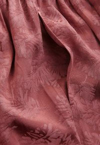 Texturerad, rostfärgad tyg med ett blommönster. Materialet verkar mjukt och något genomskinligt med en subtil lyster.
