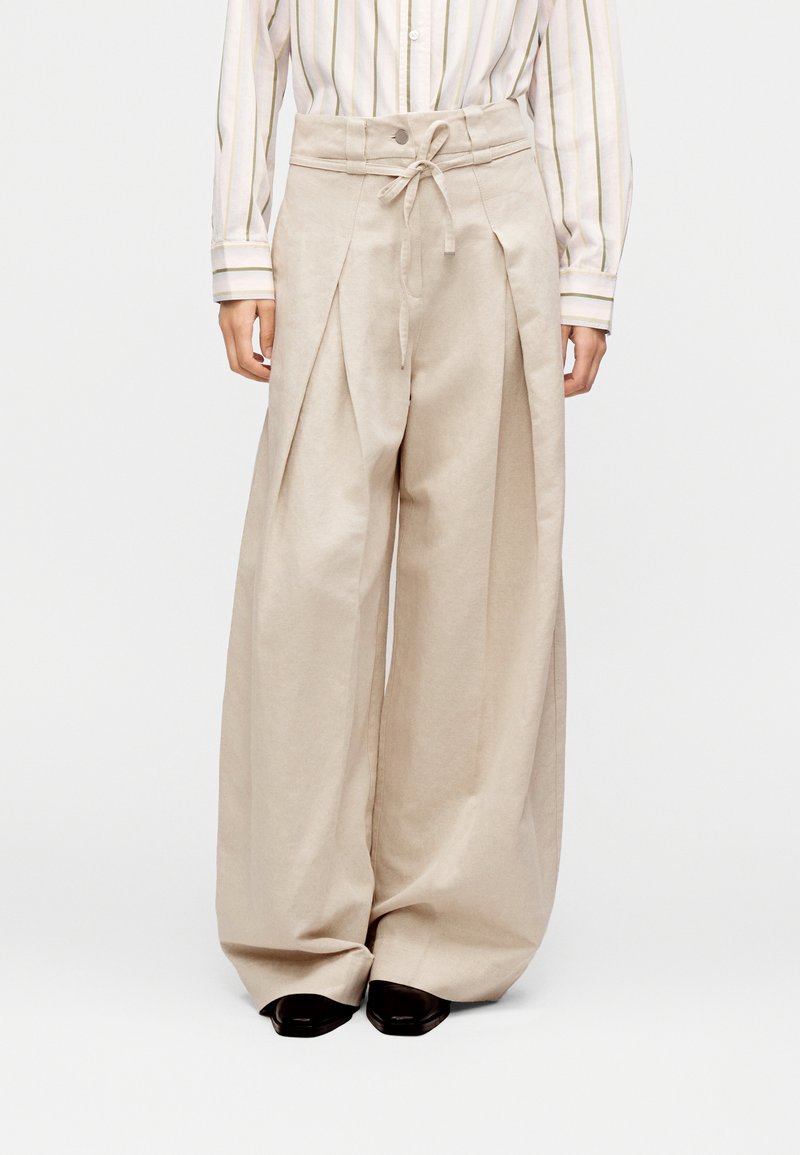 Μπεζ παντελόνια με φαρδιά ποδία από ελαφρύ ύφασμα, με ζώνη με κορδόνι, πιέτες και πλαϊνές τσέπες.