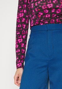 Maglietta a maniche lunghe con sfondo nero e vivace motivo floreale rosa, abbinata a pantaloni blu a quadri su misura. Tessuto texturizzato.