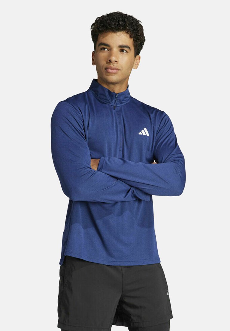Marineblauwe lange mouwen sporttop met hoge kraag, ritssluiting en wit logo op de linkerborst. Gemaakt van een gladde, rekbare stof.