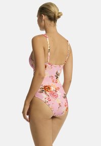 Różowy jednoczęściowy strój kąpielowy w kwiaty z cienkimi ramiączkami, z mieszanką dużych i małych wzorów kwiatowych, gładką teksturą i umiarkowanie wysokim krojem.