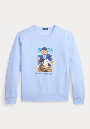 Világoskék pulóver egy grafikával, amely egy tengeri öltözetbe öltözött medvét ábrázol, aki egy széken ül, alatta a „Polo Bear by Ralph Lauren“ felirattal.