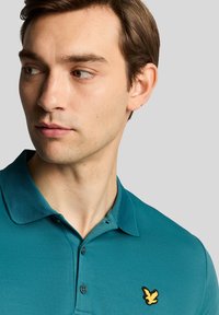 Teal polo shirt featuring a textured fabric, collar, three buttons, and a yellow bird logo on the left chest.