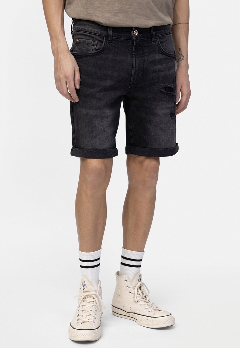Sorte denimshorts med opsmøg, som har forlommer, let slid og en bronze knaplukning. Bæres med hvide højt oppe sneakers.