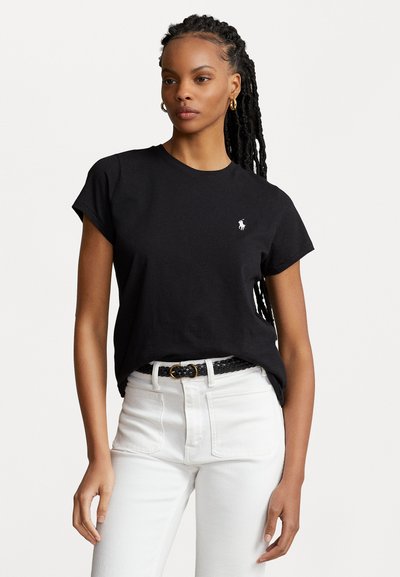T-shirt en coton noir à manches courtes roulées et col ras du cou, avec un petit logo blanc brodé sur la poitrine gauche. Assorti à un jean blanc.