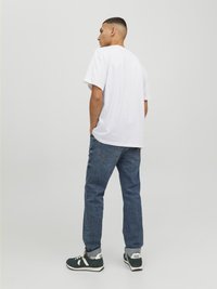 Camiseta blanca de manga corta, jeans de mezclilla azul y zapatillas verdes con acentos blancos. Ajuste casual. Vista desde la parte posterior, mostrando los detalles de la prenda.