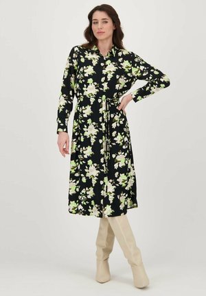 Zwarte bloemenjurk met lange mouwen, groene en witte bloempatronen, verstelbare taille. Gecombineerd met kniehoge beige laarzen. Soepele stoftextuur.