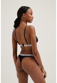 Juodas bikini komplektas su plonais petnešomis, turi kontrastingą baltą elastinę juostą, pažymėtą „Juicy Couture“ nugaroje ir ant juosmens. Lygi tekstūra.