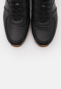 Baskets noires avec un motif crocodile texturé sur la tige, des accents en cuir lisse et une semelle en caoutchouc marron clair contrastée.