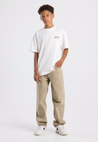 Valkoinen lyhythihainen t-paita, jossa on punaisella painettuna "NEW YORK", yhdistettynä beigeihin housuihin ja valkoisiin lenkkareihin, joissa on mustia yksityiskohtia.