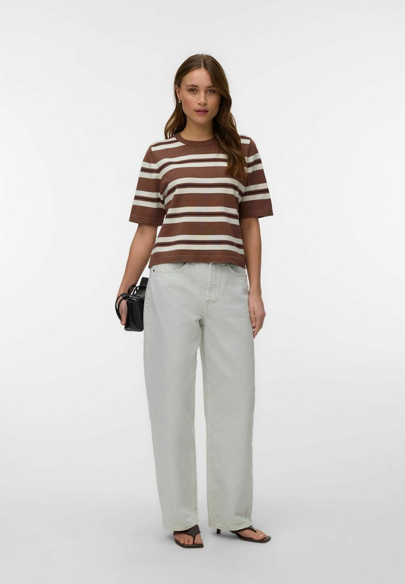 Femme portant un t-shirt à manches courtes rayé marron et blanc, un jean large gris clair, des sandales noires, et tenant un petit sac à main noir.