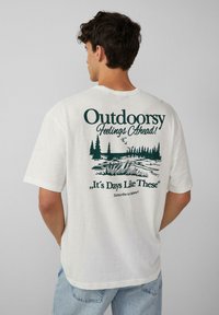 Witte katoenen t-shirt met een groene grafische print op de rug, met bomen, een meerontwerp en tekst: "Buitengevoelens Vooruit!"