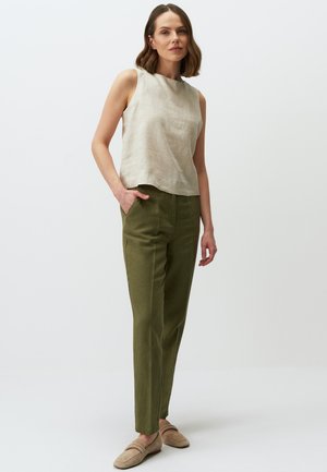 Top senza maniche in lino beige con scollo rotondo, abbinato a pantaloni dritti verdi. Il modello indossa scarpe slip-on beige chiaro.