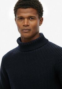 Marineblauer Rollkragenpullover aus strukturiertem Strickstoff mit einem gerippten Kragen und schmaler Passform.
