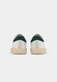 White sneakers with a beige sole, green and suede heel accents. Rounded shape with a smooth texture and minimalistic design.