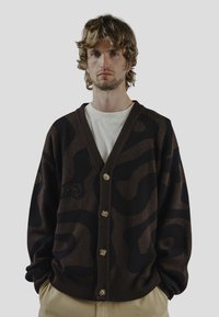 Brauner Cardigan mit einem schwarzen abstrakten Muster, mit V-Ausschnitt, fünf Knöpfen vorne und gerippten Bündchen sowie Saum.