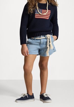 Barn iført navyblå sweater med amerikansk flag, lyse denimshorts med rebsværd, hvid perlehalskæde og navy sneakers med hvide snørebånd.
