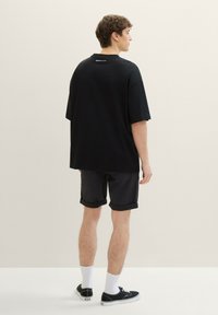 Czarna, oversize'owa koszulka wykonana z bawełny, z okrągłym dekoltem i małym logo z tyłu. Noszona z czarnymi szortami i niskimi trampkami.