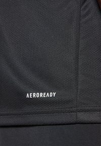 Černá sportovní tkanina s hladkým povrchem, se bílým logem "AEROREADY" na spodní části. Viditelné švy.