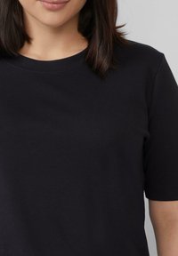 Schwarzes Kurzarm-T-Shirt aus weicher Baumwolle mit Rundhalsausschnitt und glatter Textur. Verfügt über doppelt genähte Nähte für Haltbarkeit.